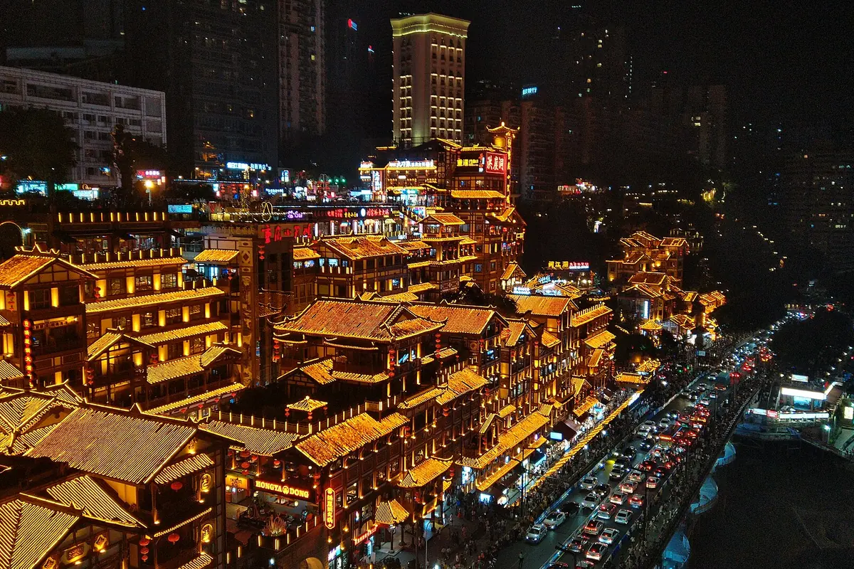 Niveauer af guldbelyste bygninger på stylter, der klatrer op ad en skråning over en vej om natten i Chongqing