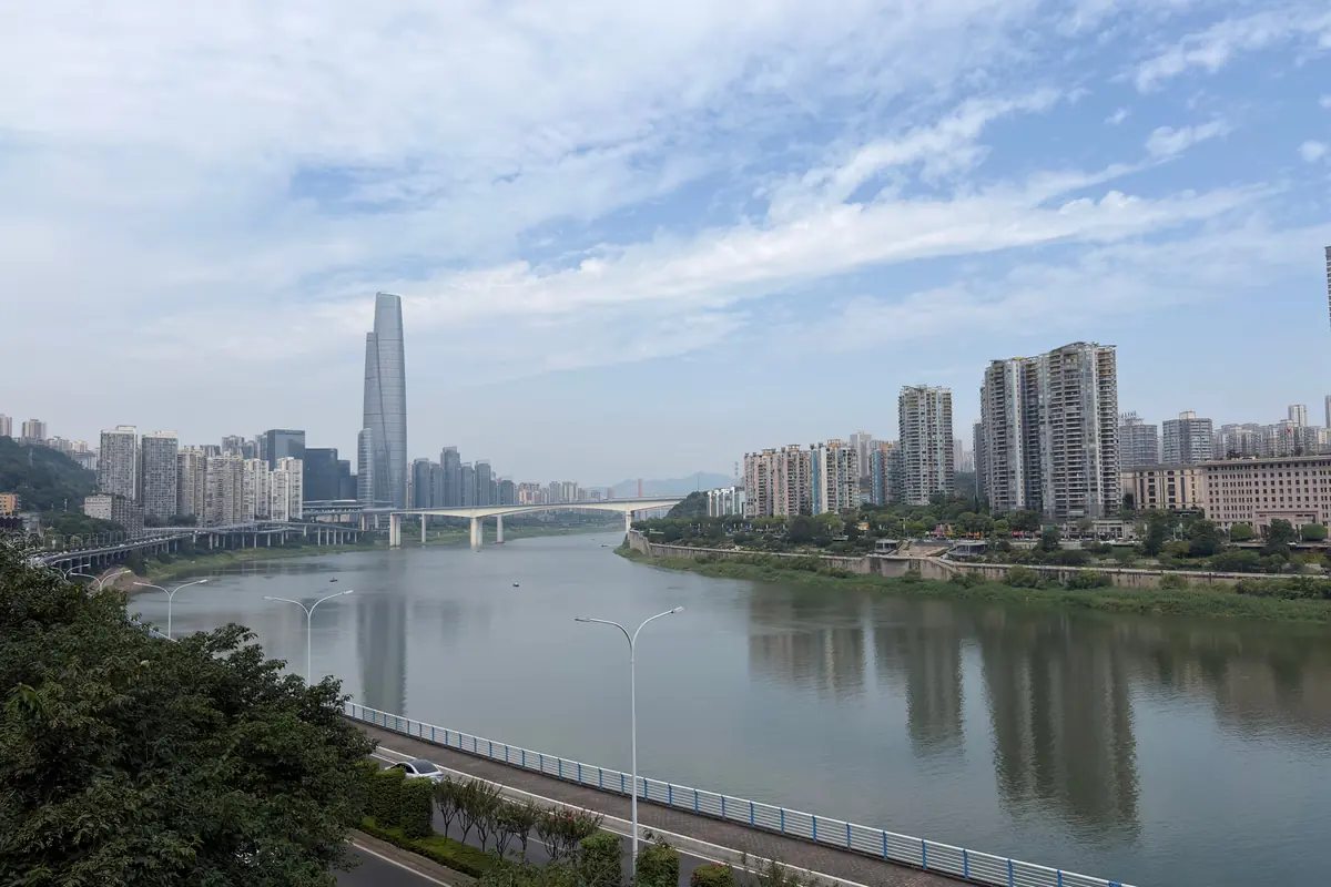 El río Jialing a la luz del día junto a las carreteras ribereñas de Chongqing, con una alta torre a lo lejos.