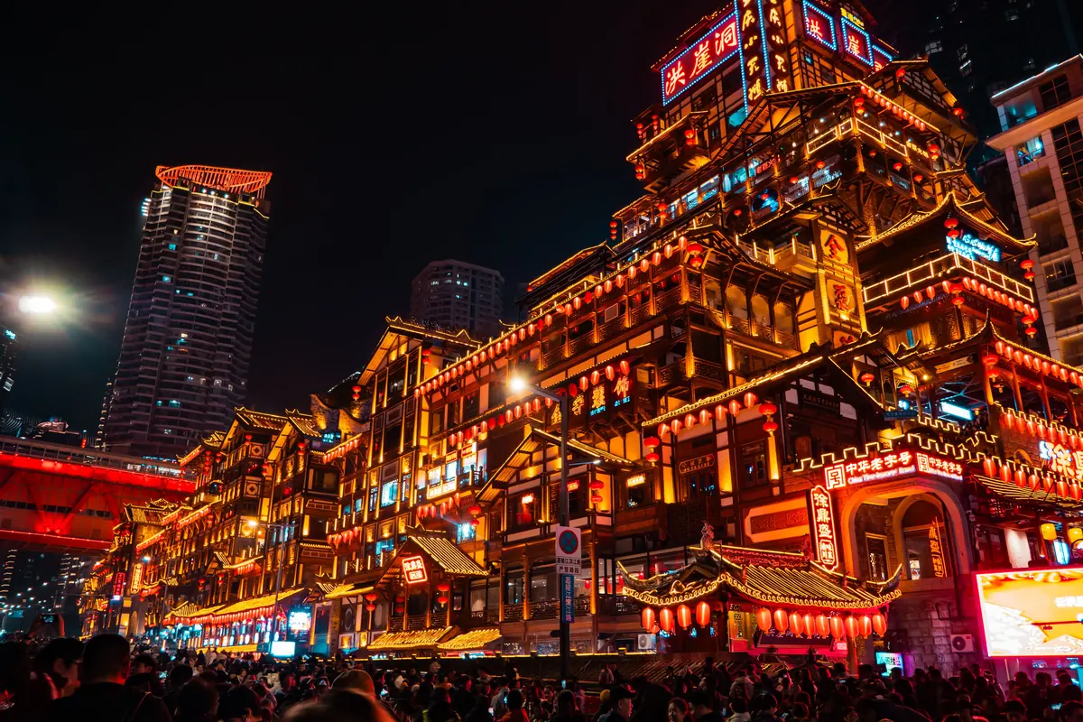 Hongya Cave iluminada en rojo y oro bajo un puente en Chongqing de noche, mostrada por su aspecto de palafito. Es un lugar distinto del teatro.