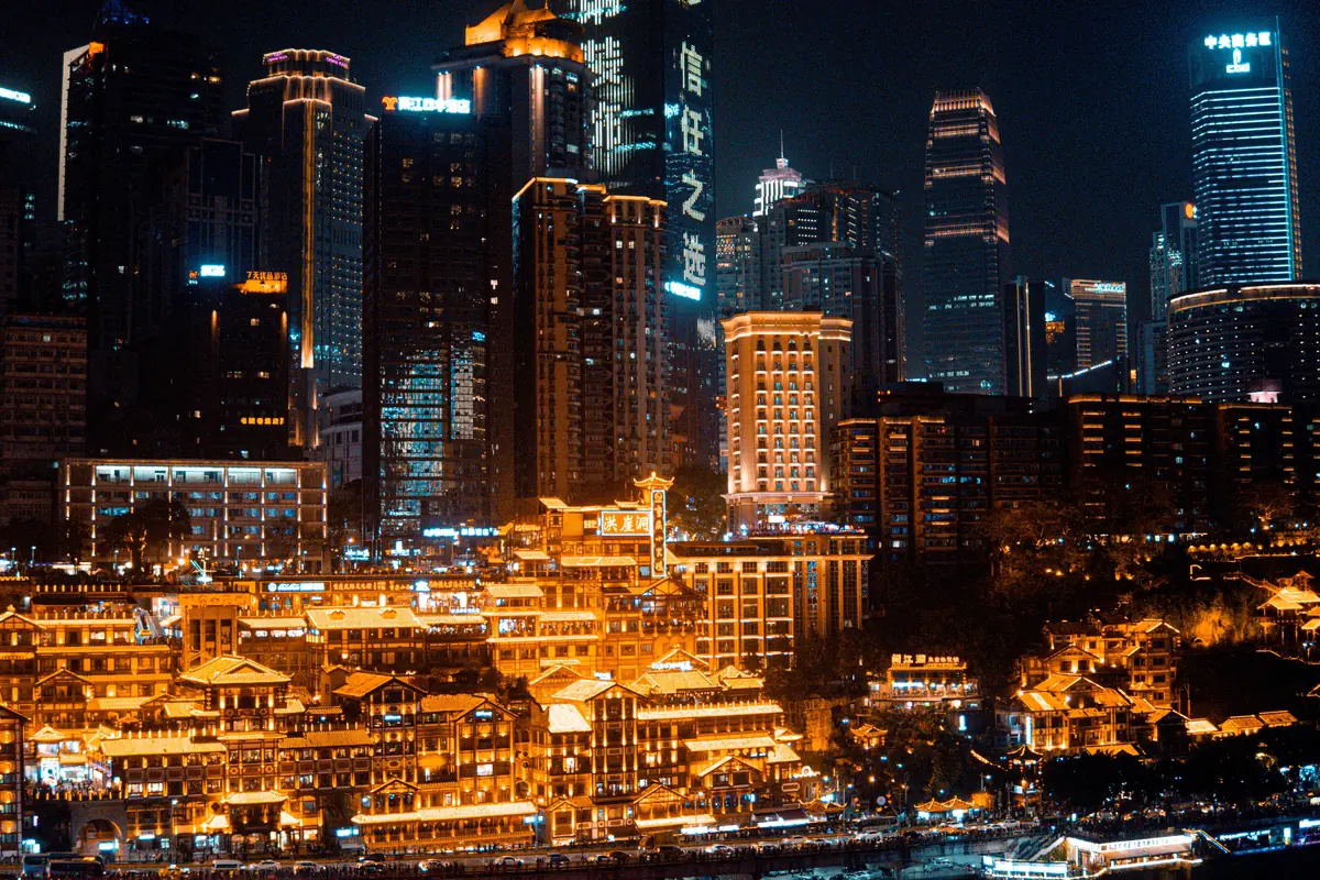 Las terrazas iluminadas en oro de Hongya Cave bajo las torres de cristal del centro de Chongqing de noche.